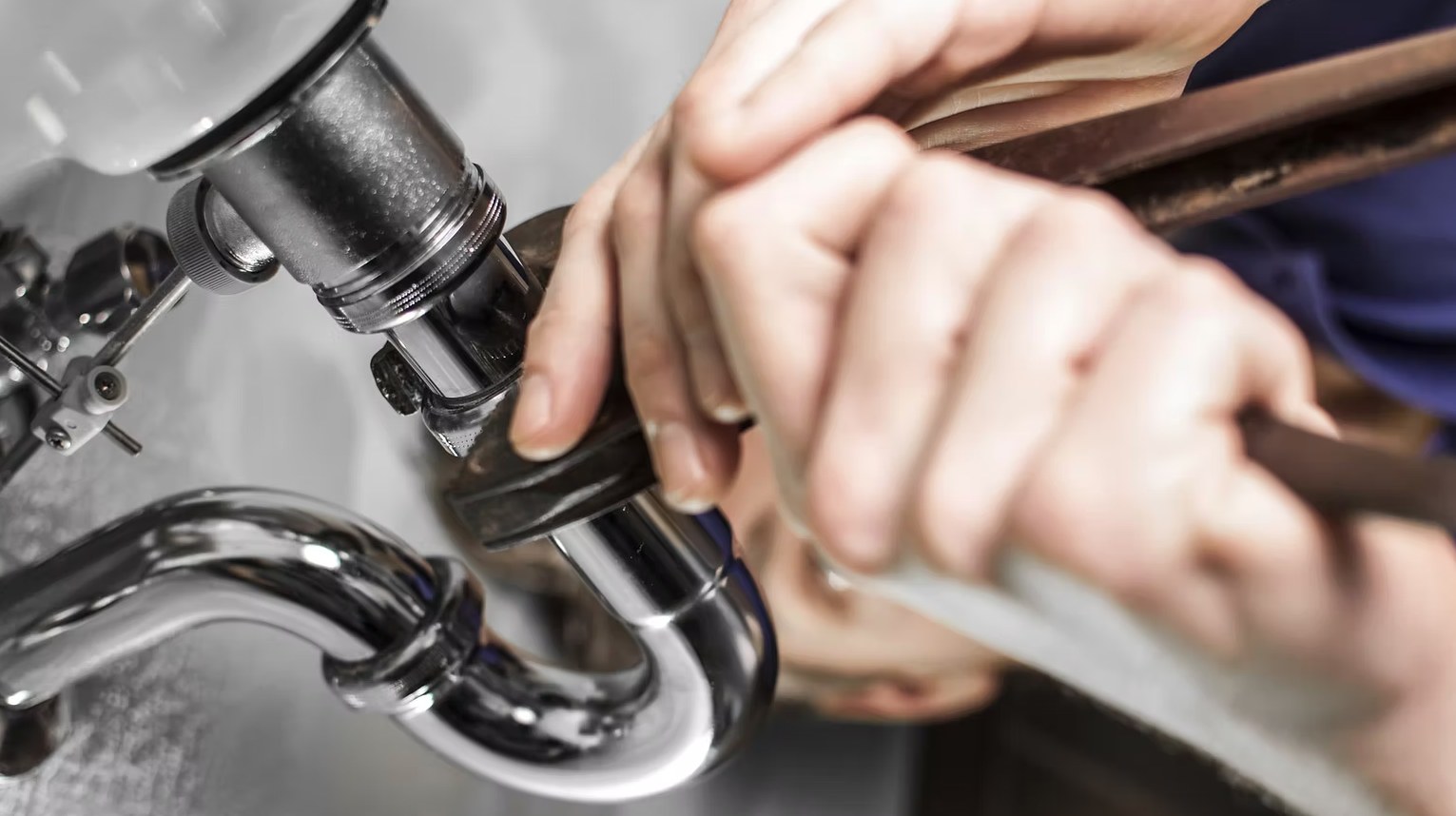 Plumber tightening a chrome pipe fitting with a wrench